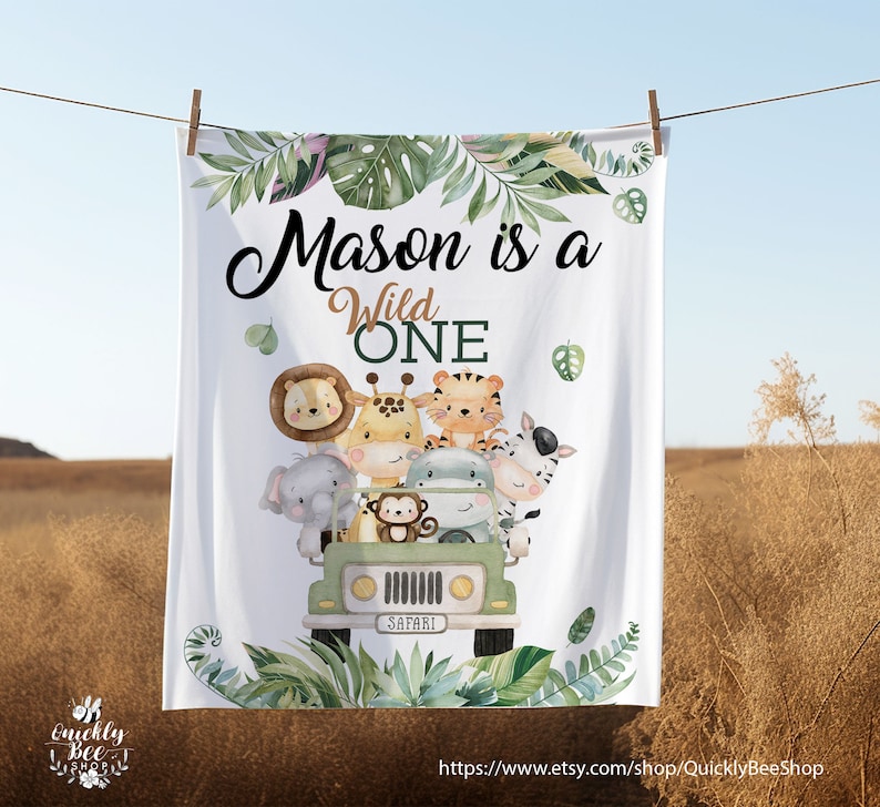 May include: White baby blanket featuring a green safari jeep and jungle animals. The text reads "Mason is a Wild One".
