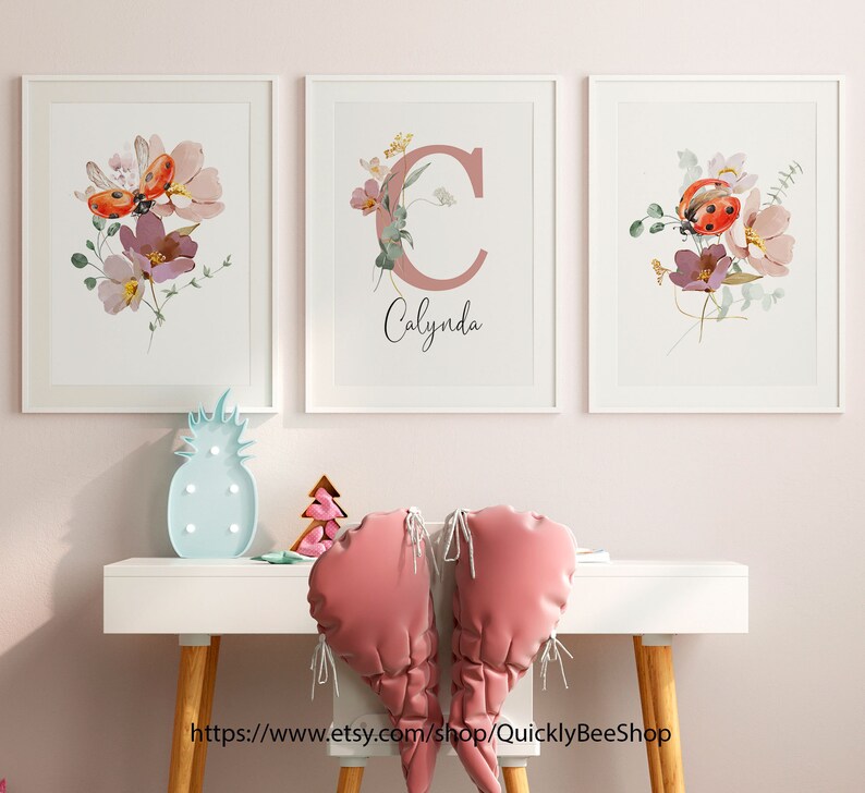 May include: Three white framed prints with watercolor floral designs and a ladybug. The middle print features the letter "C" in a pink color with the name "Calynda" written below it.