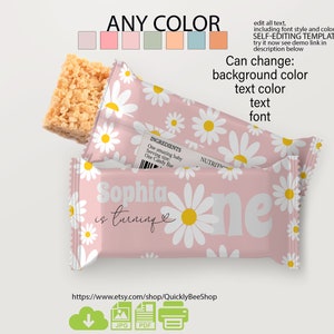 Può includere: Un involucro di barretta di caramelle rosa e bianco con un motivo di margherita. L'involucro dice "Sophia compie un anno" e ha un piccolo simbolo di cuore. L'involucro è personalizzabile con diversi colori e font.