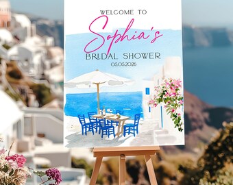 May include: A watercolor-style sign on an easel, announcing "Welcome to Sophia's Bridal Shower" with a date. The scene depicts a seaside cafe with blue chairs, tables, and an umbrella, with a backdrop of the ocean and white buildings.