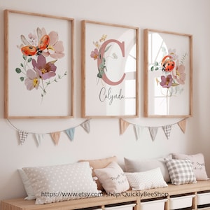 May include: Three framed prints with watercolor floral designs and ladybugs. The middle print features a pink letter C with the name "Calynda" written below.
