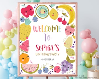 May include: A colorful welcome sign for a birthday party with a fruit theme. The sign features a variety of fruits with smiling faces, including apples, pineapples, lemons, watermelons, grapes, and cherries. The text on the sign reads "Welcome to Sophia's Birthday Party November 28".