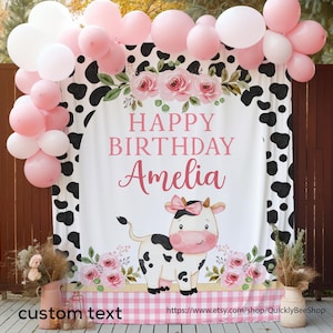 May include: A white backdrop with a black and white cow print border. The center features a pink and green floral design with a pink cow and the text "Happy Birthday Amelia".