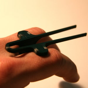 May include: A black plastic ring with a unique design, worn on a finger.