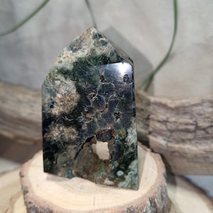 Puede incluir: Una punta de cristal verde oscuro y negro con un patrón natural único. El cristal está pulido y tiene una superficie lisa y vidriosa.