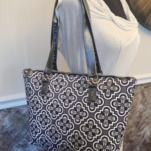 May include: A black and white patterned tote bag with black leather handles and gold hardware. The bag has a zipper closure.