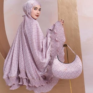 May include: A lavender prayer shawl with a geometric pattern and ruffled edges. The shawl is paired with a matching lavender handbag with a crescent moon shape.