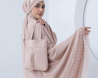Può includere: Un set di abiti da preghiera marrone chiaro, tra cui un copricapo, uno scialle e una borsa tote. Il set presenta delicate finiture in pizzo e un dettaglio a nappa sulla borsa. Il copricapo ha un'emblema color oro. Il tessuto appare morbido e fluido.