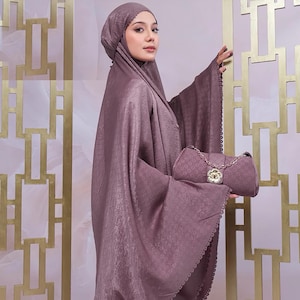 May include: A mauve-colored prayer garment set, including a head covering and a matching handbag. The set features a textured fabric and scalloped edges. The handbag has a chain strap and a decorative clasp.
