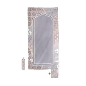 May include: A gray prayer mat with a floral design in pink, white, and brown. The mat has a central arched design and a matching carrying case. The mat is rolled up and secured with a strap.