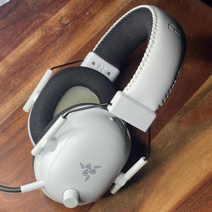 Könnte beinhalten: Weißes Gaming-Headset mit schwarzen Akzenten und einem Razer-Logo. Das Headset verfügt über ein gepolstertes Kopfband und Ohrmuscheln. Die Ohrmuscheln sind schwarz und das Kopfband ist weiß. Es hat ein eingebautes Mikrofon und einen kabelgebundenen Anschluss.