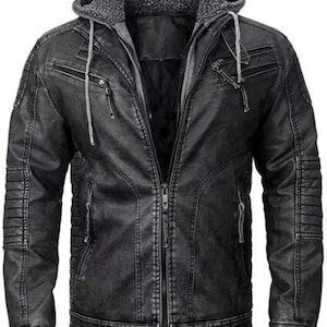 Puede incluir: Una chaqueta de cuero negra con cierre de cremallera y capucha. La chaqueta tiene un aspecto desgastado y presenta múltiples bolsillos.