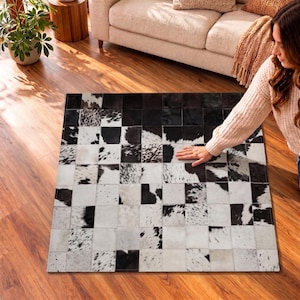 May include: A rectangular area rug composed of square patches of cowhide in varying patterns of black, white, and gray. The patches are arranged in a grid formation, featuring a mix of solid black, solid white, and speckled animal print textures.