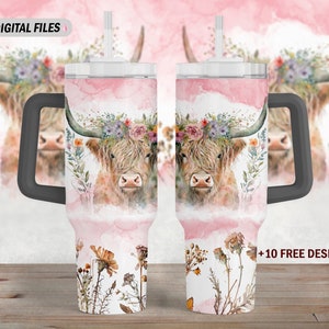 May include: Two stainless steel tumblers with a floral design featuring a Highland cow with a floral crown. The tumblers have a black handle and a straw. The background is a watercolor wash of pink and white.