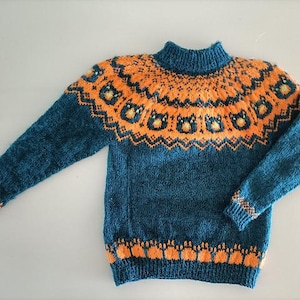 Puede incluir: Un su&eacute;ter tejido de color verde azulado y naranja con cuello alto. El su&eacute;ter presenta un patr&oacute;n geom&eacute;trico naranja alrededor del canes&uacute; y los pu&ntilde;os, con un patr&oacute;n repetido en la parte inferior. Las mangas son largas.