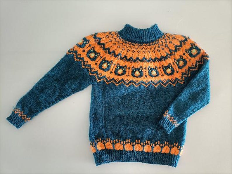 Puede incluir: Un su&eacute;ter tejido de color verde azulado y naranja con cuello alto. El su&eacute;ter presenta un patr&oacute;n geom&eacute;trico naranja alrededor del canes&uacute; y los pu&ntilde;os, con un patr&oacute;n repetido en la parte inferior. Las mangas son largas.