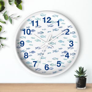 May include: White round wall clock with a blue fish pattern. The clock face features blue numerals and hands. The background is white with a repeating pattern of blue fish. The clock has a white frame.