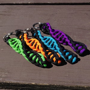 May include: Five colorful keychains with black braided rope and silver key rings. The keychains are green, orange, blue, and purple.