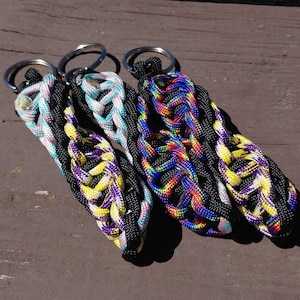 May include: Three colorful paracord keychains with black, white, yellow, purple, blue, and red accents. The keychains are made with a braided rope design and have silver key rings.