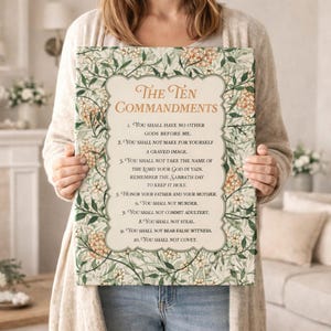 May include: A rectangular canvas print featuring "The Ten Commandments" in elegant script. The text is framed by a decorative border of green leaves and small orange flowers. The background is a light beige color.