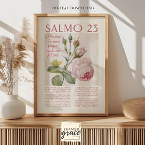 May include: A framed print with the text "SALMO 23" and a floral illustration. The print features a light pink and green color scheme, with text in a serif font. The frame is a light wood color.