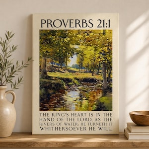 May include: A framed canvas print displaying a landscape painting of a river flowing through a forest with yellow and green trees. The text "PROVERBS 21:1" is at the top, with a Bible verse below. The print is displayed on a wooden shelf.