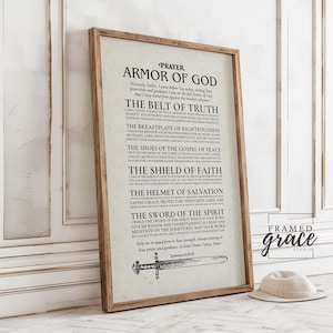 May include: A framed print with the text "Armor of God" in a rustic wooden frame. The text is arranged in a list format, with each item describing a piece of spiritual armor. A hat rests on the floor in front of the frame.