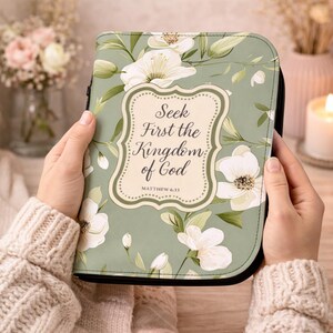 May include: A Bible cover with a floral design in shades of green and white. The cover features the text "Seek First the Kingdom of God" and the reference "Matthew 6:33". The cover has a black zipper.