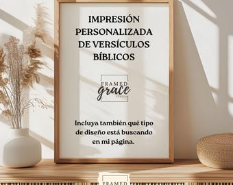 May include: A framed print with the text "IMPRESIÓN PERSONALIZADA DE VERSÍCULOS BÍBLICOS" in black. The print is in a light brown wooden frame. The logo "FRAMED grace STUDIO" is at the bottom. The print is on a wooden shelf with a vase and decorative items.