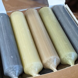 May include: Five taper candles in a box. The candles are in shades of gray, green, and brown.
