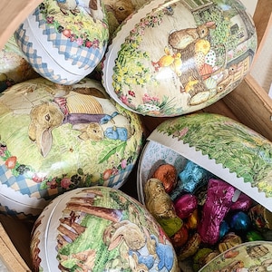 May include: A collection of Easter eggs decorated with pastel colours and images of bunnies, flowers, and other spring motifs. The eggs are made of ceramic and have a glossy finish.