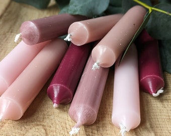 Puede incluir: Un grupo de ocho pequeñas velas de té en tonos rosa y burdeos. Las velas están dispuestas en un racimo sobre una superficie de madera.