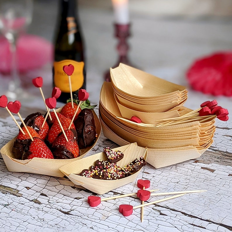 May include: A set of wooden bowls with a stack of small bowls and a larger bowl. The bowls are arranged on a white surface with chocolate covered strawberries and chocolate hearts.