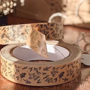May include: A roll of brown packing tape with a floral pattern printed in black. The tape is on a wooden surface.