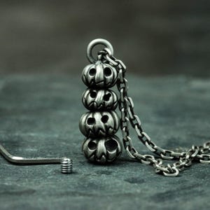 May include: A silver necklace with a pendant of four stacked jack-o'-lantern faces.