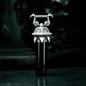 May include: A silver bottle stopper with a detailed design resembling a medieval tower. The stopper has a handle with a twisted design and a pointed top.