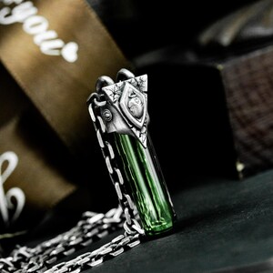 May include: A silver pendant necklace with a green glass vial and a detailed silver design. The pendant is attached to a silver chain.