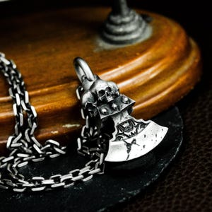 以下が含まれることがあります： 詳細な斧のデザインとスカルモチーフが特徴のシルバーカラーのペンダントネックレス。 斧の頭には複雑な模様があり、シルバーチェーンに接続されています。 ペンダントの長さは約4cmです。