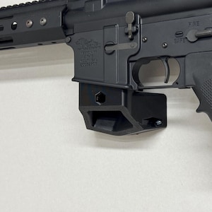 May include: Black AR-15 style rifle with a black polymer lower receiver, a black handguard, and a black pistol grip. The rifle has a safety selector switch labelled "SAFE" and "FIRE".