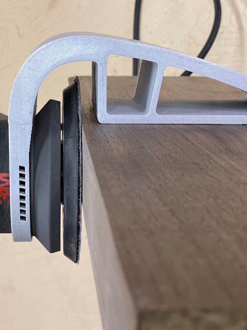 May include: A gray 3D printed sanding jig with a sanding pad attached to a power sander. The jig is designed to help sand edges and curves.