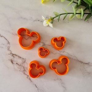 Puede incluir: Conjunto de cinco cortadores de galletas de plástico naranja con forma de cabeza de Mickey Mouse. Los cortadores son de diferentes tamaños.
