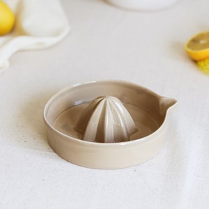 May include: A beige ceramic citrus juicer with a ridged center for squeezing lemons or limes.