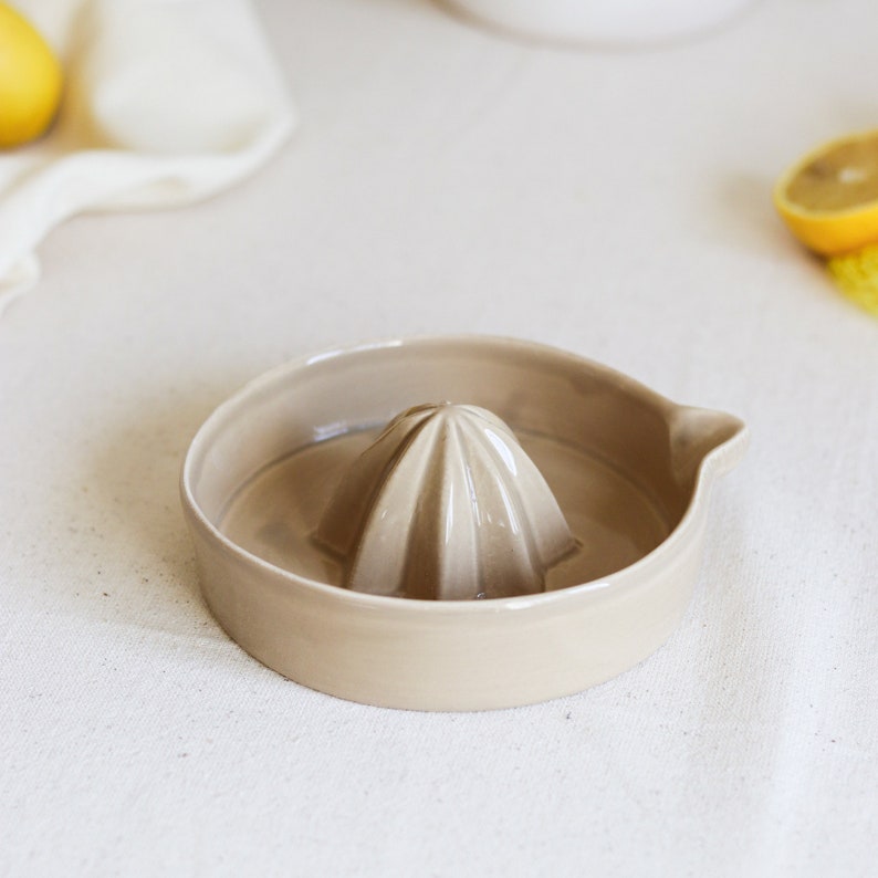 May include: A beige ceramic citrus juicer with a ridged center for squeezing lemons or limes.