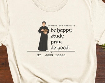 May include: A white t-shirt with a black illustration of a man holding a book. The text on the shirt reads "formula for sanctity be happy. study. pray. do good. ST. JOHN BOSCO"