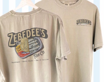 May include: Khaki t-shirt with a graphic print of a can of sardines and the text "Zebedee's Fish Co. Capernaum - North Shore - Sea of Galilee".