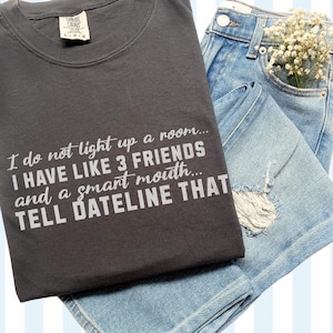 May include: A dark gray t-shirt with a white graphic print that reads "I do not light up a room... I have like 3 friends and a smart mouth... Tell Dateline that."