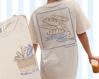 May include: A beige t-shirt with a graphic of bread and fish on the back and a basket of bread and fish on the front. The text "Matthew 14:20" is printed on both sides of the shirt.
