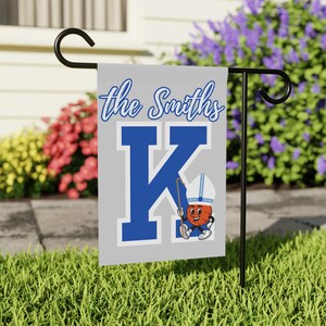 May include: A gray garden flag with the text "the Smiths" and a blue "K" with a cartoon basketball player holding a shovel.