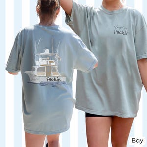 May include: A light blue t-shirt with a graphic of a boat on the back and the text "Long Live Pookie" on the front.