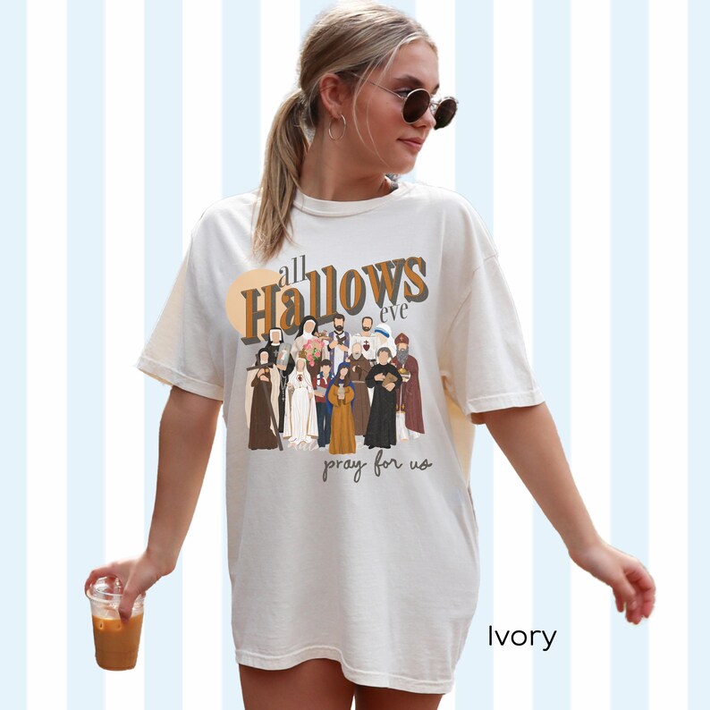 K&ouml;nnte beinhalten: Ein wei&szlig;es T-Shirt mit einem grafischen Druck einer Gruppe von Personen in religi&ouml;ser Kleidung. Der Text "all Hallows eve pray for us" ist auf das T-Shirt gedruckt. Das T-Shirt ist mit "Ivory" gekennzeichnet.
